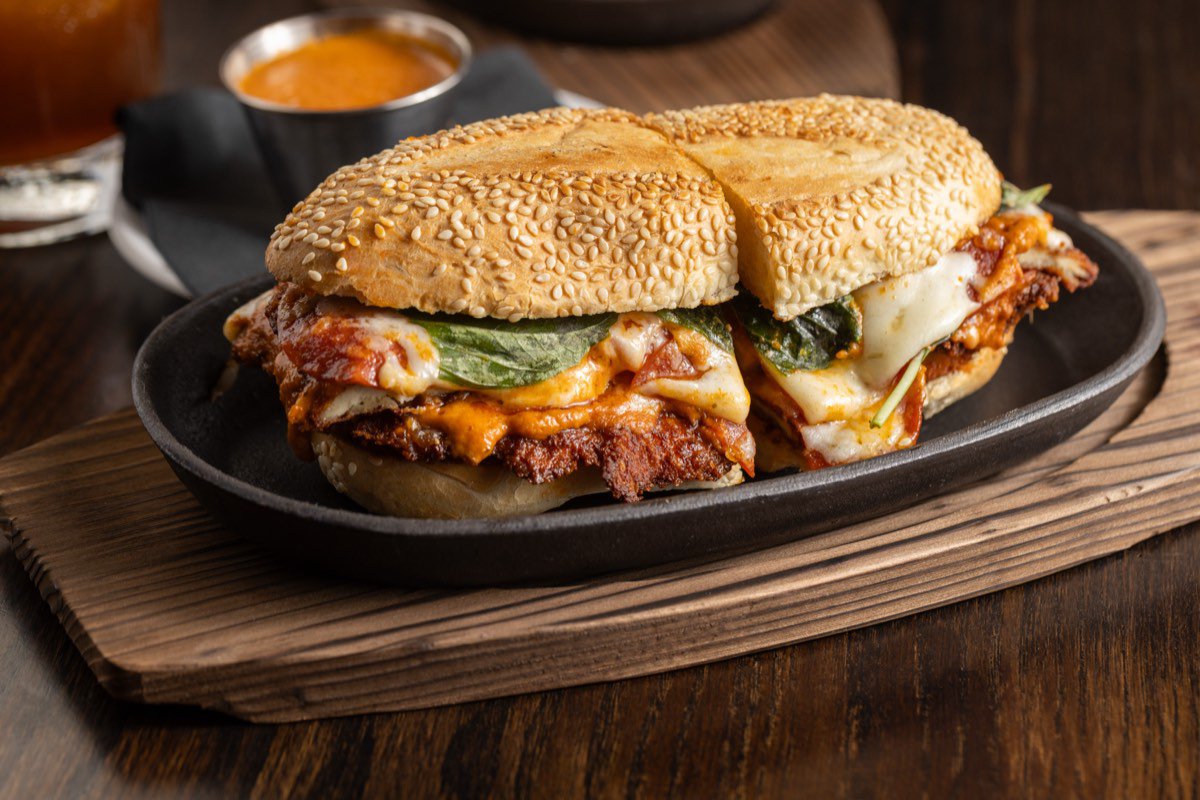 A chicken cutlet sandwich with vodka sauce, pepperoni, melted cheese and Thai
                    basil on a seeded roll, served in a cast iron dish.