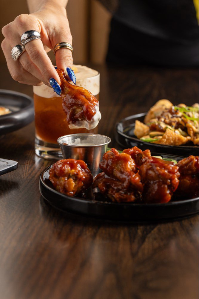 A Chicago BBQ chicken wing being lifted from a black dish and dipped into dill ranch.