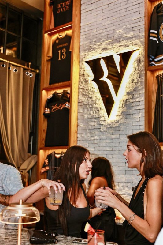 Two guests at the bar beside the framed jerseys and the glowing V.