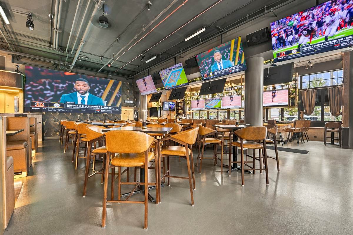 The big-screen room set before doors, leather chairs at high-tops under a wall of screens.