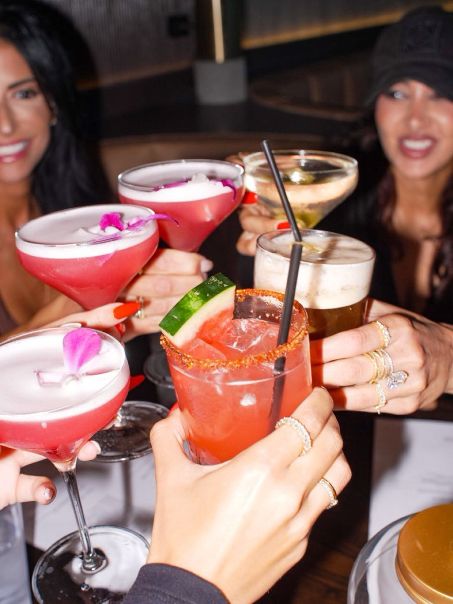 Six cocktails raised together over the table.