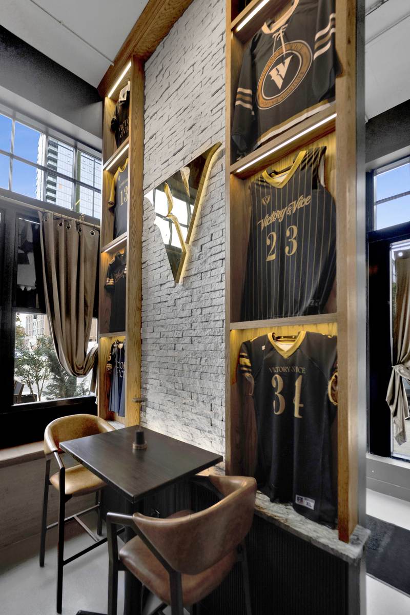 Framed jerseys and a lit V on white brick beside a high-top for two.