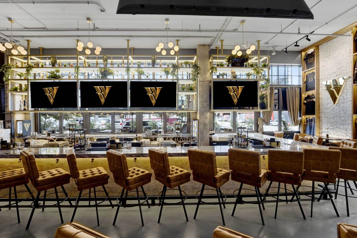 The full length of the bar, gold quilted stools beneath a row of screens.