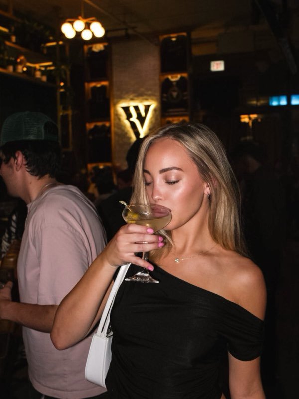 A martini raised in front of the lit V on the back wall.