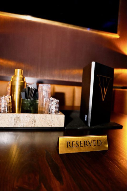 A brass RESERVED card on a table set with glassware and a shaker.