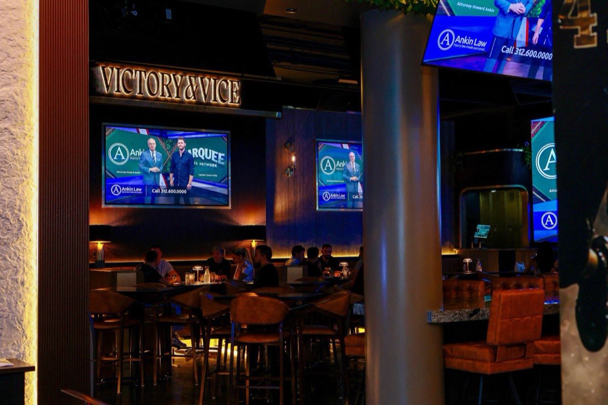 The room from the doorway, screens lit and the Victory & Vice sign above the bar.