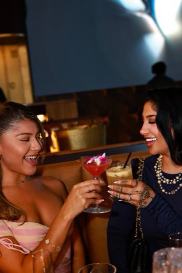 Two guests laughing over cocktails in a booth.