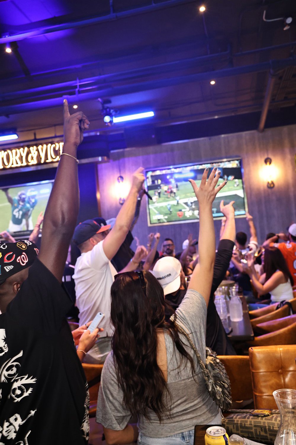 Arms up across the room for a touchdown, the game on every screen under the Victory & Vice sign.
