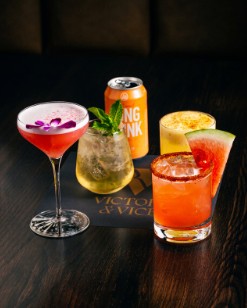 Signature cocktails on the bar: a coupe with an orchid, a mint highball, a watermelon cocktail and a can.