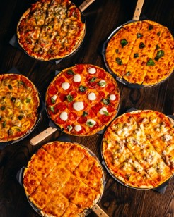Six pizzas on paddles across the table.