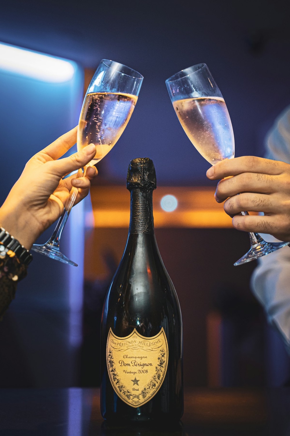 Two glasses of champagne raised over a bottle of champagne.