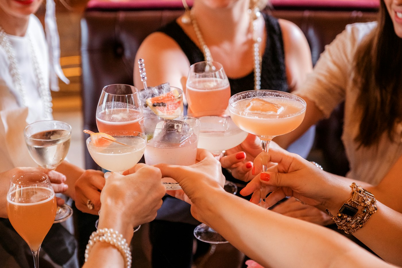 Friends clinking coupe glasses of pink cocktails across a table.