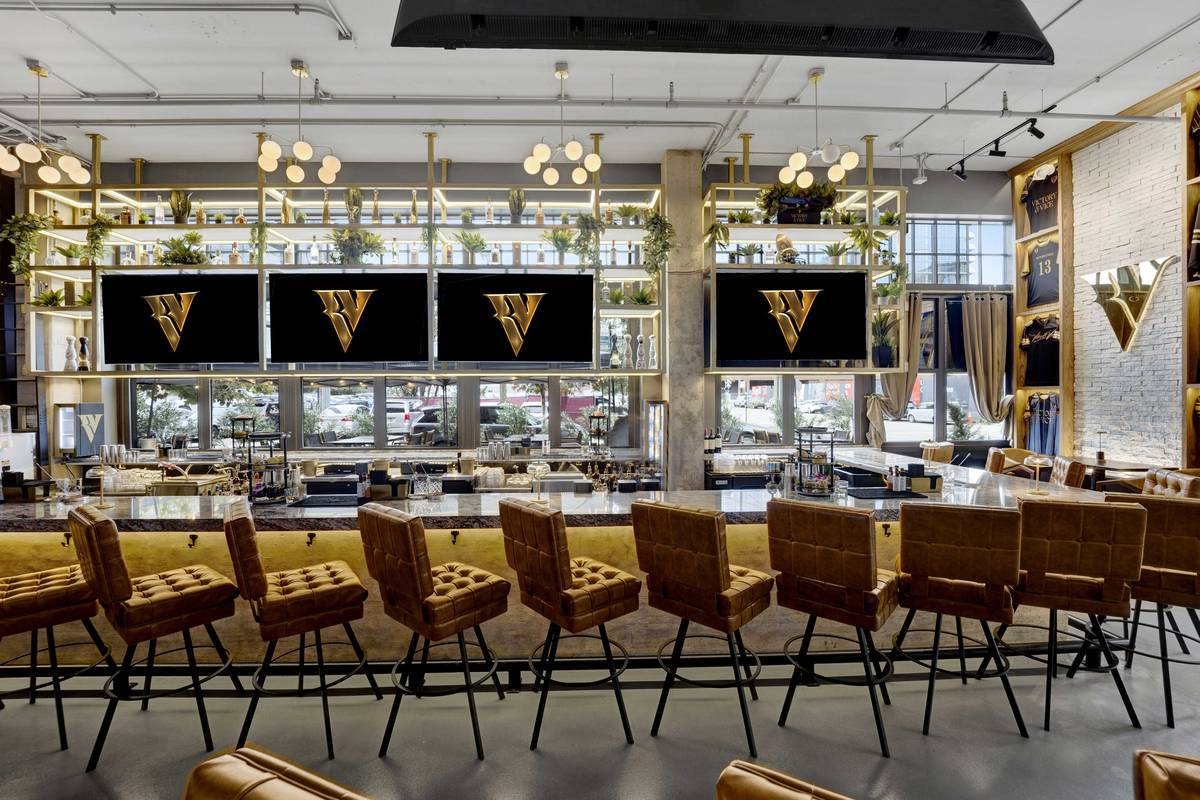The full length of the bar, gold quilted stools beneath a row of screens.